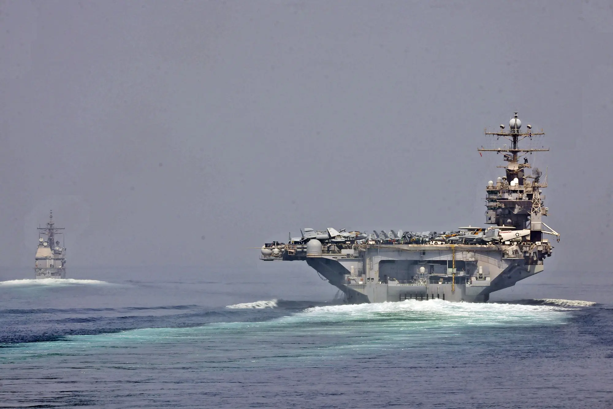 Two US Navy warships sailing through the Strait of Hormuz with a tanker in the distance